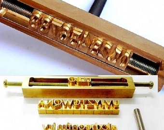 May include: A set of brass letter stamps and a holder. The stamps are arranged in a wooden holder with a screw mechanism. Additional stamps and a screw are also visible. The letters are in a serif font.