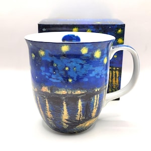 Peut inclure: Une tasse en céramique arborant une reproduction d'une scène nocturne avec un ciel bleu foncé, des étoiles jaunes et des reflets dorés sur l'eau. Le motif inclut une silhouette de voilier et une boîte assortie avec un bord intérieur blanc.