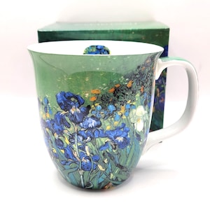 Pode incluir: Uma caneca de cerâmica com uma reprodução vibrante da pintura Lírios de Vincent van Gogh. O exterior apresenta flores azul-escuras com caules e folhagem verdes sobre um fundo verde. O interior é branco com um pequeno motivo de lírio.
