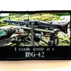 Peut inclure: Un écusson noir avec une image d'une mitrailleuse MG-42 sur un fond vert et marron. Le texte "I sexually identify as a MG-42" est imprimé en blanc en dessous. Le patch a une bordure noire.