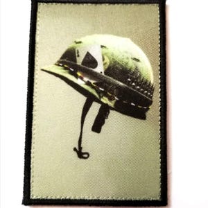 Peut inclure: Écusson rectangulaire représentant un casque militaire vert avec une étoile blanche. Le casque est doté d'une jugulaire noire sur un fond vert clair. Le patch est bordé d'une couture noire.