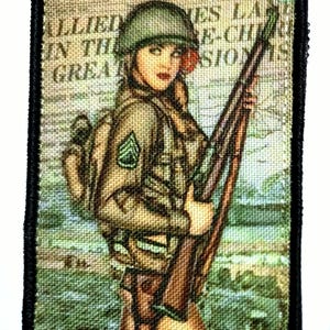 Può includere: Toppa ricamata con un'illustrazione vintage di una soldatessa in uniforme, con fucili. La toppa ha un bordo nero e il testo "ALLIED IN THE GREAT".