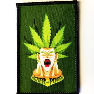 May include: A rectangular green patch with a black border. It features a cartoon character with a cannabis leaf headdress and the words "HIGHER POWER". The character has an open mouth.