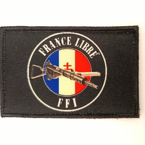 Peut inclure: Un écusson rectangulaire noir avec un emblème circulaire. L'emblème affiche les mots "FRANCE LIBRE" et "FFI", un design bleu, blanc et rouge, et une mitraillette au centre.