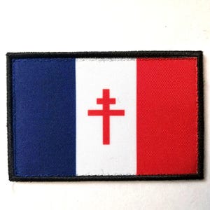Pode incluir: Remendo retangular com o desenho da bandeira francesa e uma cruz de Lorena vermelha. O remendo tem uma borda preta. As cores são azul, branco e vermelho. Provavelmente para roupas ou acessórios.