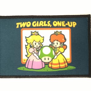 Peut inclure: Écusson rectangulaire avec un fond bleu foncé et une bordure noire. L'écusson présente une image de dessin animé de deux princesses tenant un champignon vert avec le texte "TWO GIRLS, ONE-UP" en jaune.