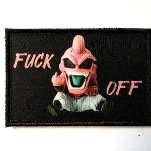 Può includere: Toppa rettangolare nera con un personaggio dei cartoni animati con la pelle rosa, occhiali da sole e un gesto del dito medio. Le parole "FUCK OFF" sono stampate in rosa.