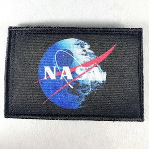 以下が含まれることがあります： NASAのロゴが入った黒い長方形のパッチ。ロゴには、白と青のディテールが入った青い球体、「NASA」の文字、赤いスウッシュが含まれています。パッチには黒い縁取りがあります。