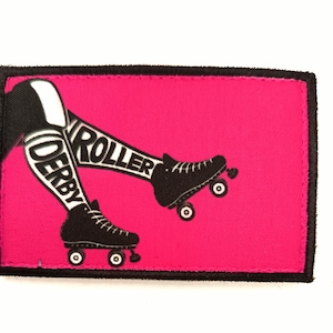 Peut inclure: Un écusson rectangulaire avec un fond rose vif et une bordure noire. L'écusson présente une illustration stylisée de jambes et de patins à roulettes de roller derby, avec les mots "ROLLER DERBY" en blanc.