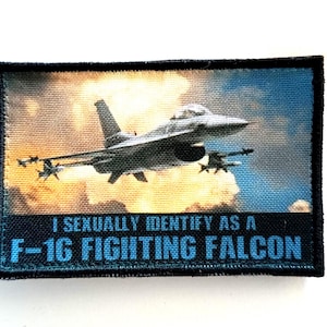 May include: A rectangular patch with an image of an F-16 Fighting Falcon jet in flight, set against a sky and cloud background. The text "I SEXUALLY IDENTIFY AS A F-16 FIGHTING FALCON" is printed in blue at the bottom.