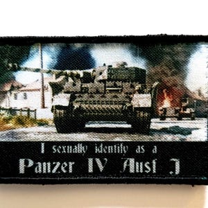 Może przedstawiać: Czarna prostokątna naszywka z wizerunkiem czołgu wojskowego na tle płonącego tła. Tekst "I sexually identify as a Panzer IV Ausf J" jest wydrukowany na dole naszywki na biało.