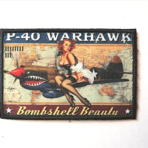 May include: A rectangular patch featuring a vintage pin-up girl seated on a P-40 Warhawk airplane. The patch has the text "P-40 WARHAWK" at the top and "Bombshell Beauty" at the bottom. The background includes a map.