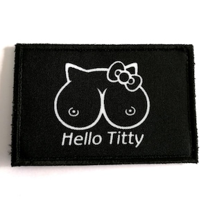 Peut inclure: Écusson rectangulaire noir avec un dessin blanc d'un visage de chat et de seins, avec un nœud papillon. Le texte "Hello Titty" est en dessous. L'écusson est sur fond blanc.