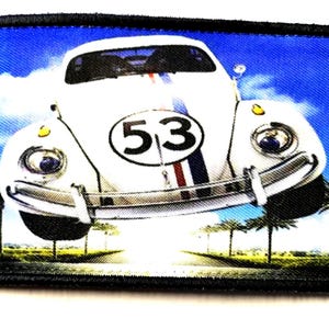 May include: A rectangular patch featuring a white Volkswagen Beetle with the number "53" on the front. The car has blue and red stripes and is set against a blue sky with palm trees and a road.