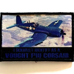 Peut inclure: Écusson rectangulaire avec un avion Vought F4U Corsair bleu en vol. Le texte "I SEXUALLY IDENTIFY AS A VOUGHT F4U CORSAIR" est affiché en bleu. Bordure noire.