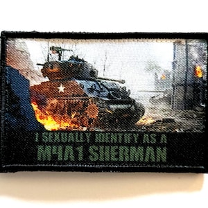 Puede incluir: Un parche rectangular con un tanque militar en una escena de guerra con llamas. El texto "I SEXUALLY IDENTIFY AS A M4A1 SHERMAN" está impreso en verde sobre un fondo negro.