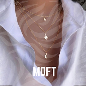 Könnte beinhalten: Mehrreihige goldfarbene Halskette mit Anhängern in Form von Stern, Sonnenstrahl und Mond. Die Halsketten werden über einem weißen Hemd getragen. Das Wort "MOFT" wird in weißen Blockbuchstaben am unteren Bildrand angezeigt.