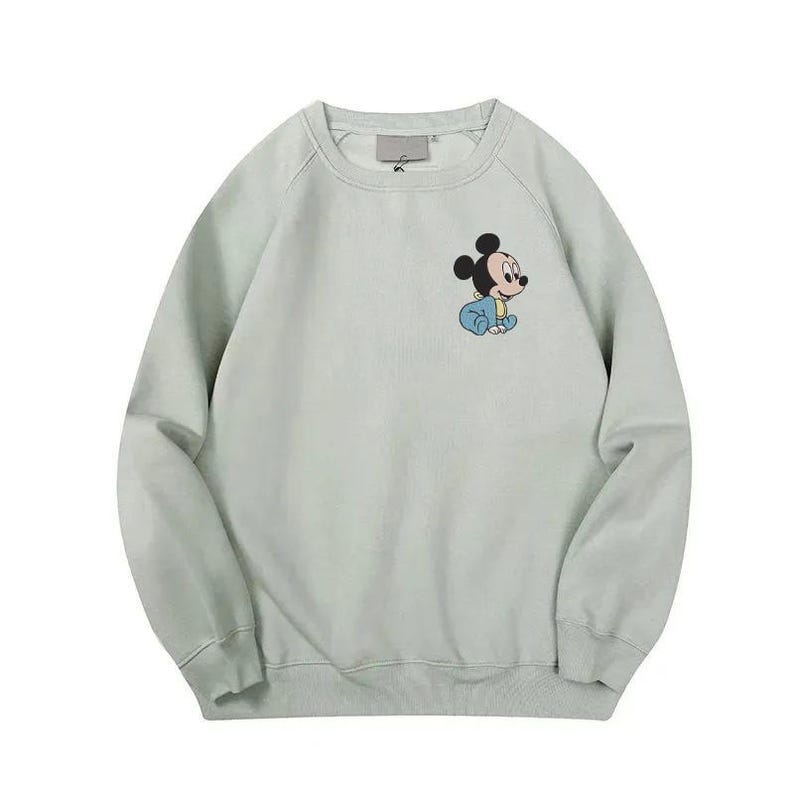 Pode incluir: Um moletom verde claro com um pequeno gr&aacute;fico do Mickey Mouse em azul beb&ecirc;. O moletom tem gola redonda e mangas compridas. O desenho est&aacute; na &aacute;rea do peito esquerdo.