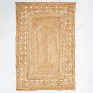 Peut inclure: Tapis rectangulaire en jute de couleur beige naturel. Le tapis présente un motif géométrique avec un rectangle central et une bordure de cercles reliés. Il est fait de fibres de jute tissées, créant une surface texturée.