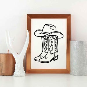 May include: Black and white line art print of a cowboy hat resting on top of a pair of cowboy boots. The boots have decorative stitching. The artwork is in a gold-colored frame.