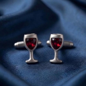 May include: A pair of silver-toned cufflinks shaped like wine glasses, each featuring a deep red, faceted gemstone set into the bowl of the glass. The cufflinks have a smooth, matte metallic finish and a standard T-bar fastening mechanism.