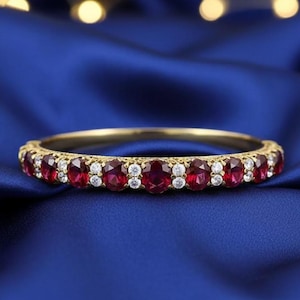 May include: A gold bracelet featuring alternating oval-cut red and small white gemstones. The bracelet is set against a deep blue background, with soft lighting.