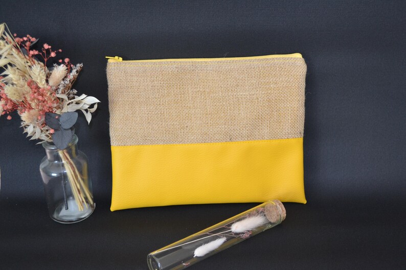 May include: A rectangular pouch with a natural burlap top and a bright yellow bottom. The pouch has a gold zip closure. A clear glass vase with dried flowers and a glass tube with dried flowers are also in the image.