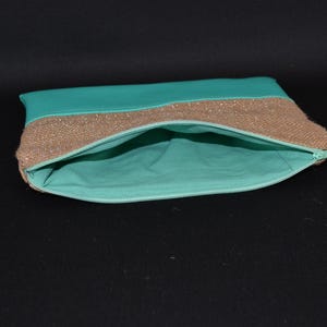 May include: An open turquoise clutch bag with a gold sequined band and a turquoise interior. The zip is a matching turquoise colour. The bag is on a black background.