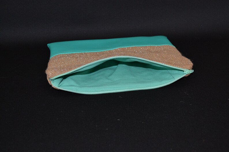 May include: An open turquoise clutch bag with a gold sequined band and a turquoise interior. The zip is a matching turquoise colour. The bag is on a black background.