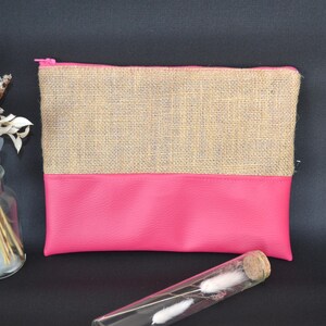 May include: A rectangular pouch with a pink base and a tan burlap top, secured with a pink zip. A clear glass vial with white decorative elements and a small glass vase with dried flowers are in the foreground.