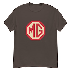 Puede incluir: Una camiseta marrón con un diseño octogonal rojo y crema con las letras "MG". La camiseta tiene mangas cortas y cuello redondo. El gráfico está centrado en el pecho.