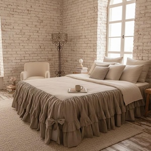 Könnte beinhalten: Ein Schlafzimmer mit einem Bett, das mit Bettwäsche in neutralen Tönen bezogen ist, einschließlich eines gerüschten Bettrocks. Der Raum verfügt über eine Backsteinmauer, ein Bogenfenster, einen Teppich, eine dekorative Stehlampe und einen Stuhl.
