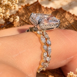 May include: A gold ring featuring a large rectangular radiant-cut centre stone with a halo of small round diamonds. The band is adorned with a double row of marquise-cut diamonds set in gold, creating a detailed and sparkling appearance.