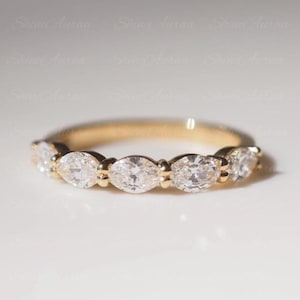 May include: A gold band ring featuring five marquise-cut clear stones set in a row. The metal band has a polished finish, and the stones are secured with small prongs. The design showcases a continuous arrangement of faceted gems across the front.
