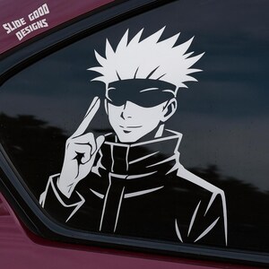 May include: White vinyl decal of an anime character with spiky hair and a blindfold, pointing a finger upwards. The decal is applied to a car window. The text "SLIDE GOOD DESIGNS" is in the upper left corner.