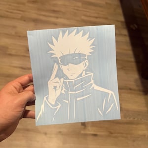 May include: White vinyl decal featuring a stylized anime character with spiky hair and a blindfold. The character is making a hand gesture. The decal is on a light blue background.