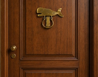 May include: A dark brown wooden door featuring a brass whale-shaped door knocker mounted in the center. The door has a rectangular panel design, a round brass doorknob, and a matching keyhole plate located on the left side of the door frame.