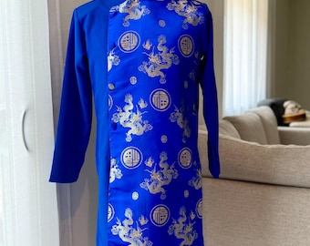 Op de afbeelding: Een helderblauwe tuniek met lange mouwen, een mandarijnkraag en gouden draken- en symboolpatronen. De tuniek wordt op een mannequin getoond, waarbij het traditionele ontwerp en de op maat gemaakte pasvorm worden benadrukt. Het kledingstuk is een cultureel item.