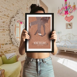 Puede incluir: Una impresión rectangular enmarcada con fondo marrón y una ilustración gráfica de dos pares de piernas bailando. El texto "NEW ORLEANS JAZZ CLUB" está impreso en blanco en la parte inferior, con patrones de texto circulares alrededor.
