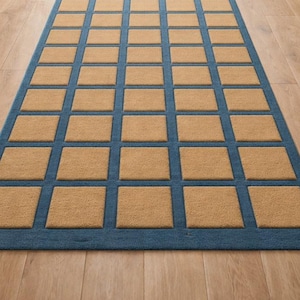 May include: A rectangular rug with a blue border and a grid pattern of tan squares. The rug is placed on a wooden floor, with a view of a garden through open doors.