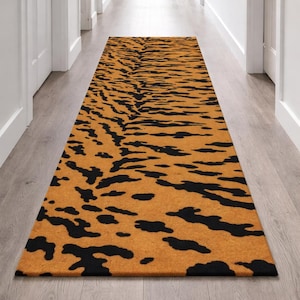 May include: A rectangular runner rug with a tiger stripe pattern. The rug features a tan background with black stripes. The rug is placed in a hallway with light wood flooring and white doors.
