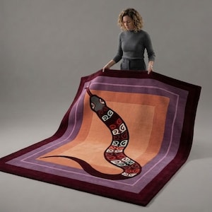 Puede incluir: Una alfombra rectangular con un motivo central de serpiente con patrones geométricos blancos sobre un cuerpo rojo oscuro. La alfombra tiene un diseño de borde en capas en tonos naranja, morado claro y burdeos, creando un efecto de marco.