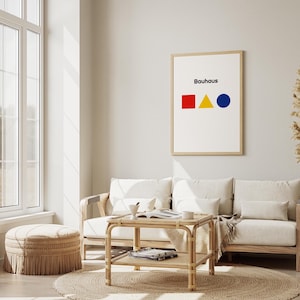 Può includere: Una stampa artistica Bauhaus incorniciata con un quadrato rosso, un triangolo giallo e un cerchio blu sotto la parola "Bauhaus". L'opera d'arte è appesa sopra un divano bianco, un tavolino intrecciato e un tappeto rotondo.
