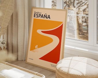 May include: Framed poster with the text "Vuelta a España" in black. The poster features a cyclist on a winding road design in orange, red, and beige. The words "La Vuelta" and "First Edition Discipline" are also visible.