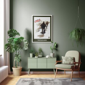 Könnte beinhalten: Ein gerahmter Druck mit dem Titel "THE FALKLANDS" zeigt Figuren in einer verschneiten Landschaft mit einer britischen Flagge. Der Druck hängt an einer grünen Wand, über einem grünen Schrank. Ein Stuhl mit einem Camouflage-Kissen ist in der Nähe.