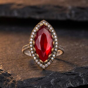 Anello autentico con taglio marquise effetto rubino, contorno di zirconi, montatura in rame color oro e fascia in argento.
