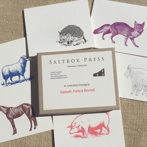 May include: A set of six assorted letterpress cards featuring animal illustrations in various colors. The designs include a fox, sheep, goat, horse, pig, and hedgehog. The cards are packaged in a small, rectangular box with the text "SALTBOX PRESS".