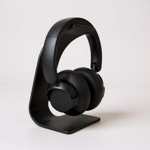 Könnte beinhalten: Ein mattschwarzer Over-Ear-Kopfhörer auf einem geschwungenen schwarzen Ständer. Der Kopfhörer verfügt über einen soliden Kopfbügel und runde Ohrmuscheln mit dem eingeprägten Wort Edifier an der Seite. Der Ständer hat ein glattes, bogenförmiges Design.