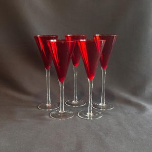 May include: Five elegant red wine glasses with long stems and flared bowls. The glasses are arranged in a group, showcasing their vibrant color and sleek design. The clear stems and bases contrast with the deep red of the bowls, creating a sophisticated look.