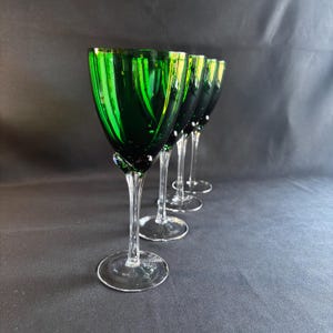 May include: Four green wine glasses with clear stems and bases are arranged in a row. The glasses have a textured, swirled design and a vibrant emerald color. The stems are slender, and the bases are round.